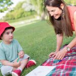 A happy moment between a mother and child drawing outdoors on a picnic blanket.